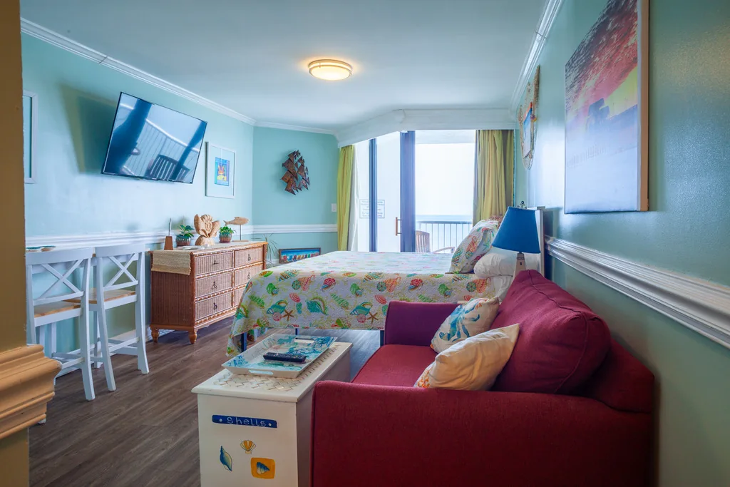Studio living area with sofa, dining table, king bed, and oceanfront doors